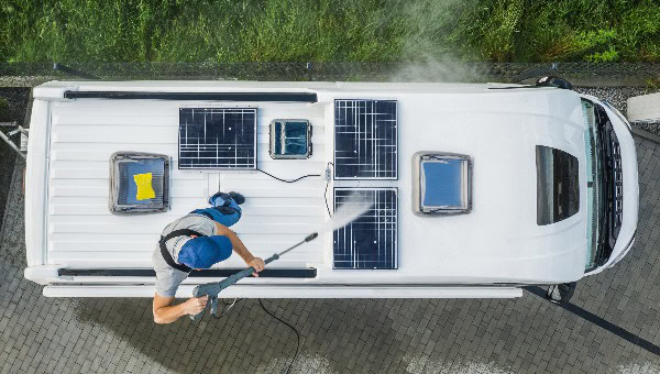 Mann reinigt mit Hochdruckreinigung RV Camper; Van Dach mit Solarpanels ausgestattet